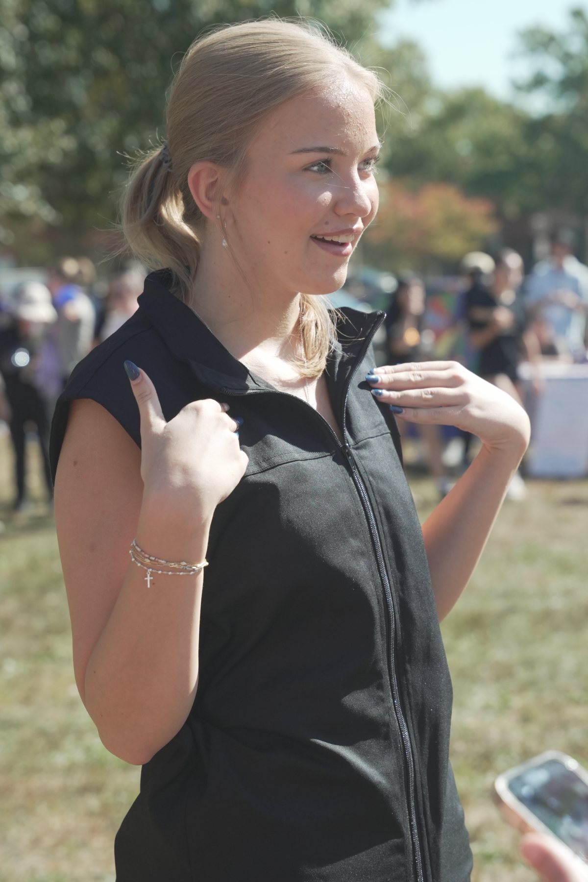 A young woman smiling and pointing to the Tactus vest she is wearing at an outdoor event